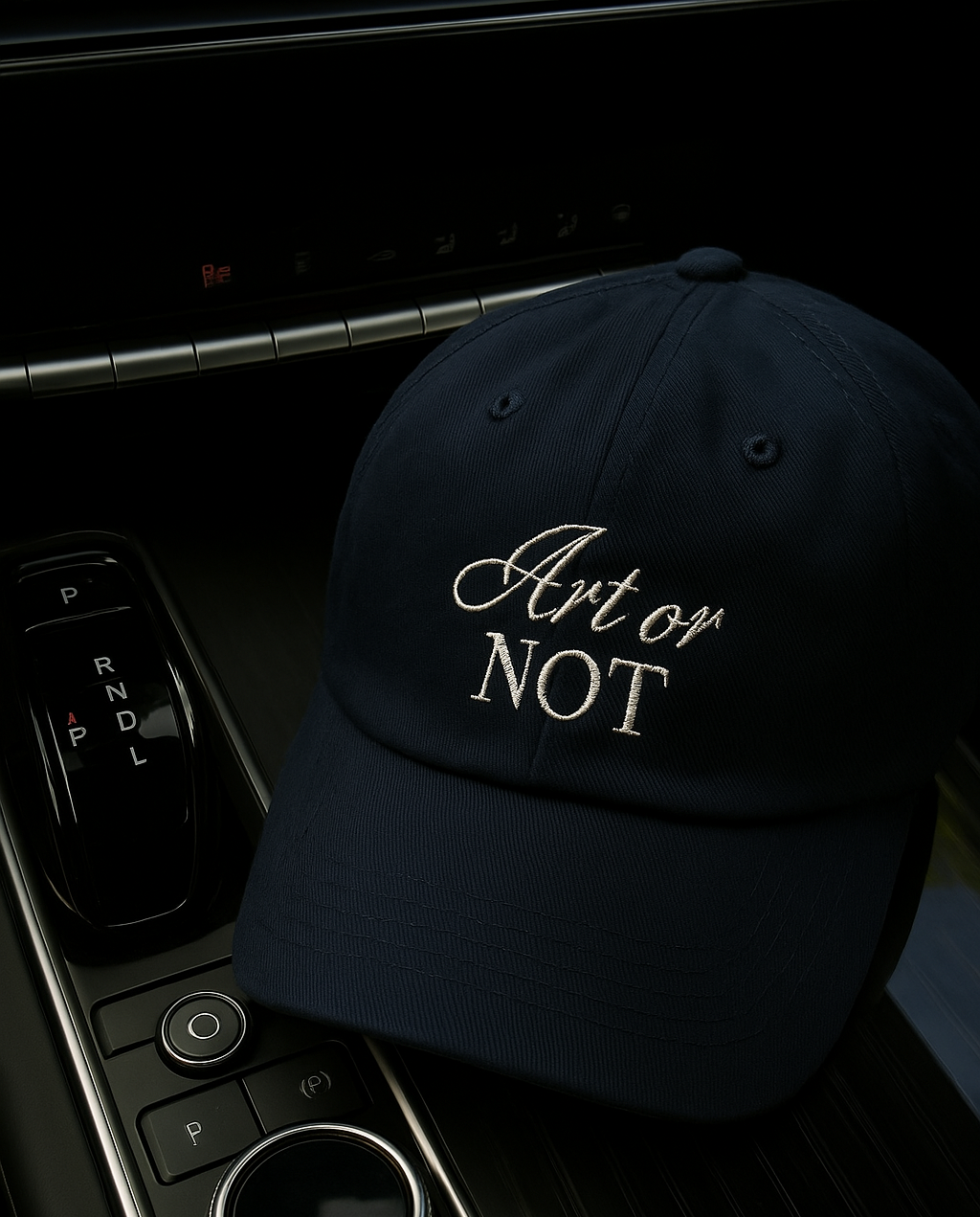 Close up of navy blue baseball cap on car dashboard, featuring embroidered phrase: “Art or Not”