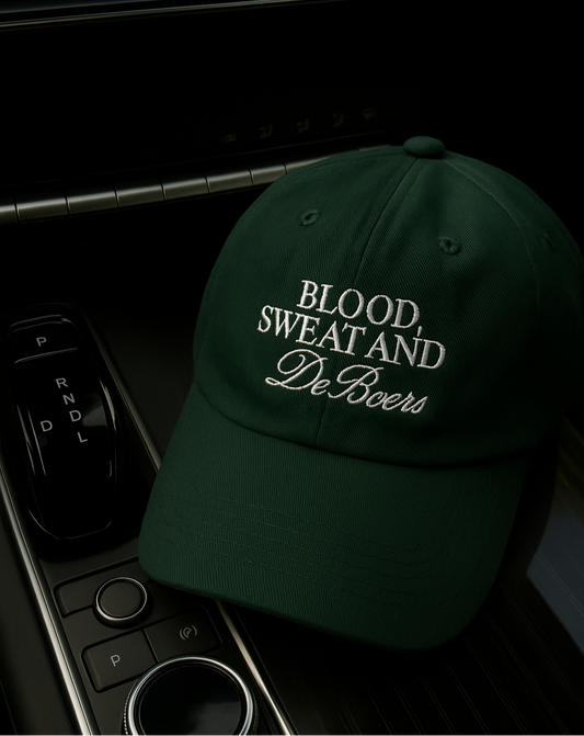 Ivy green embroidered baseball cap for women with “Blood, Sweat & DeBeers" text, photographed inside a car interior