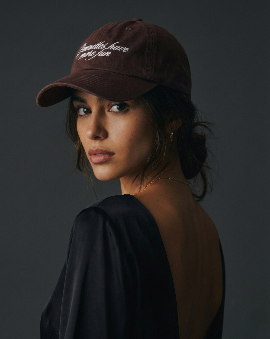 Woman wearing a brown embroidered baseball cap with “Brunettes Have More Fun” text